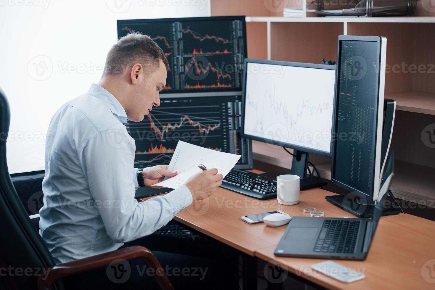 Reading the report. Man working online in the office with multiple computer screens in index charts photo