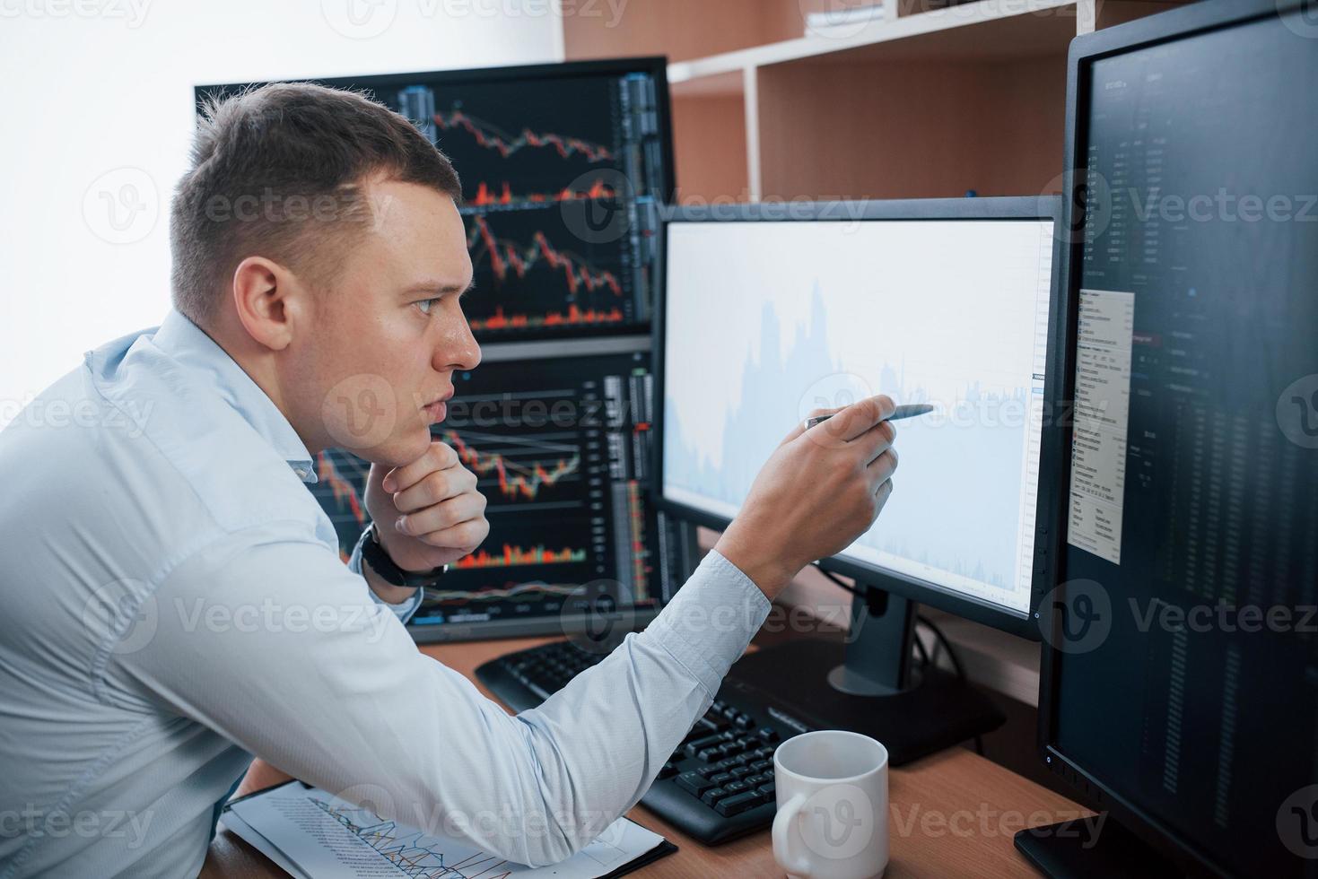 Checks information. Man working online in the office with multiple computer screens in index charts photo
