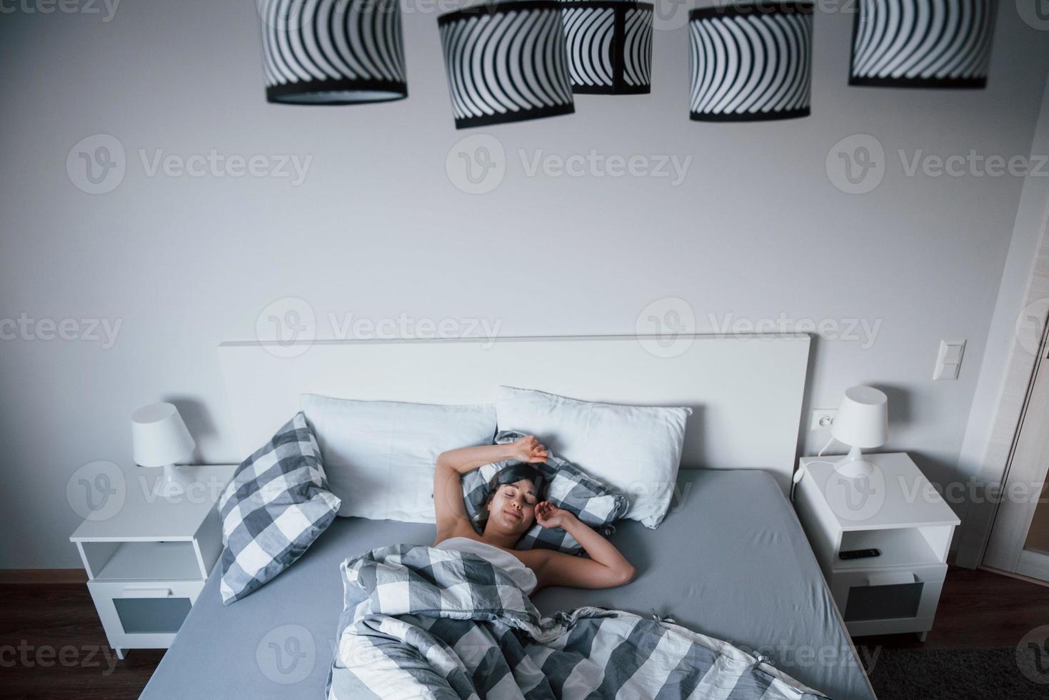 Weekends has come. Woman with blindfold mask for a sleep is lying on the bed at morning time photo