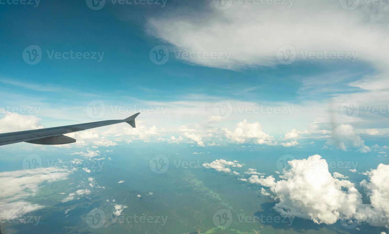 vista desde el interior del avión a través de la ventana del avión sobre el cielo azul, las nubes blancas y la montaña verde. vuelo de aerolínea comercial para viajes de verano. ala de avión sobre la ciudad. avión volando por encima de la tierra. foto