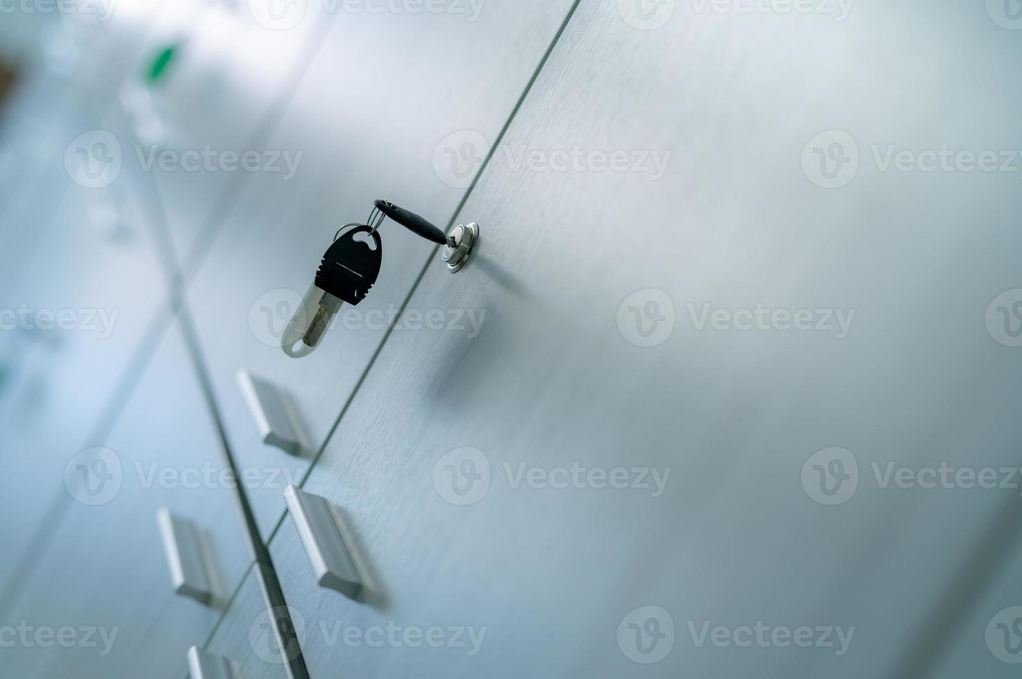 Locker with key in office room. Filing cabinet lock with key for safety and security system in public facility. Secure lock system for document files in business office. White locker door for storage. photo