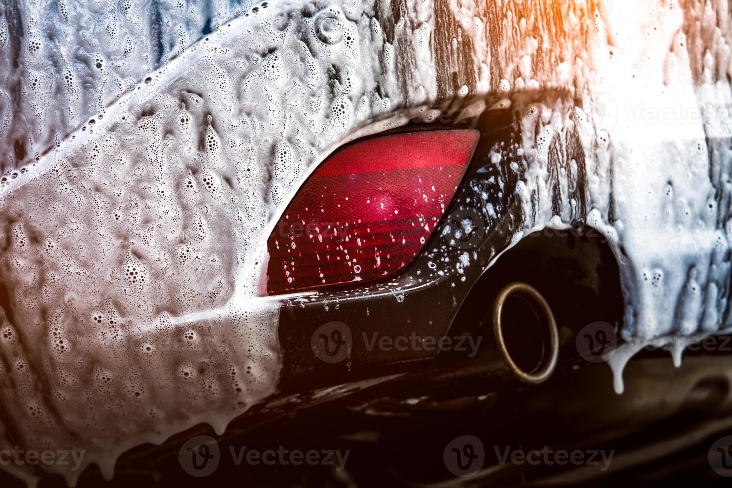 Blue compact SUV car with sport and modern design washing with soap. Car covered with white foam. Car care service business concept. Car wash with foam before glass waxing and glass coating automobile photo