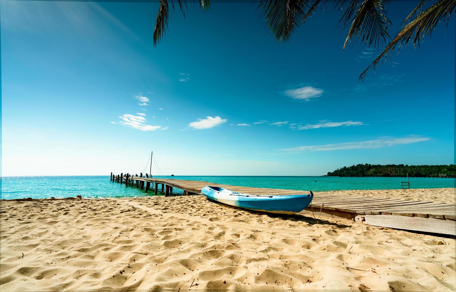 Beautiful view tropical paradise beach of resort. Coconut tree, wooden bridge, and kayak at resort on sunny day. Summer vacation concept. Summer vibes. Golden sand beach of resort with blue sky. photo