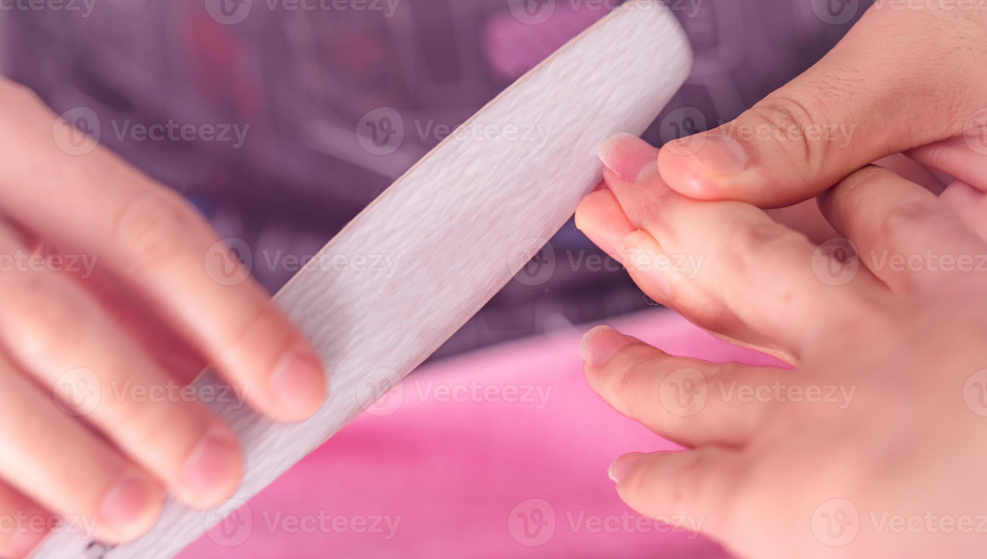 Woman receiving fingernail manicure service by professional manicurist at nail salon. Beautician