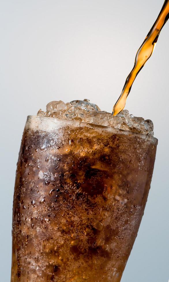 Closeup of soft drink pouring to glass with crushed ice cubes isolated on white background with copy space. There is a drop of water on the transparent glass surface. photo