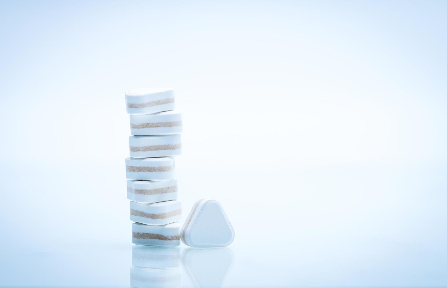 Macro shot of triangle shape tablet pills. Three layers tablet pills for indication antacid, digestive and gastric pain. Group of sandwich tablets pills on white background with copy space for text. photo