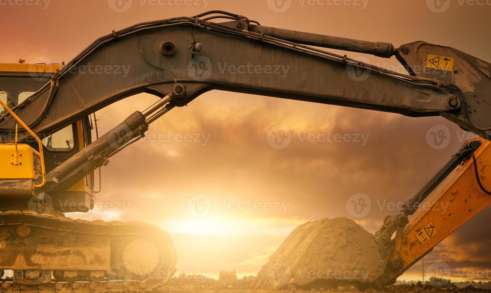 Backhoe parked at construction site after digging soil. Bulldozer on sunset sky and clouds background. Digger after work. Earth moving machine at construction site at dusk. Digger with dirt bucket. photo