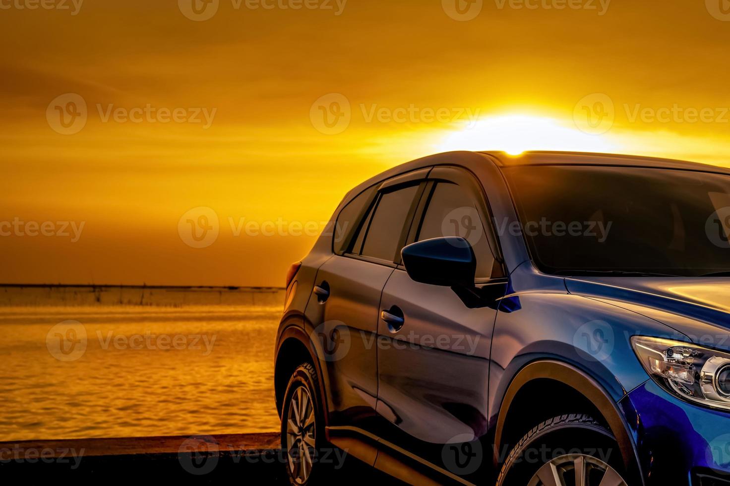 Blue compact SUV car with sport and modern design parked on concrete road by the sea at sunset. Business success concept. Road trip travel. Automotive industry. Electric and hybrid car technology. photo