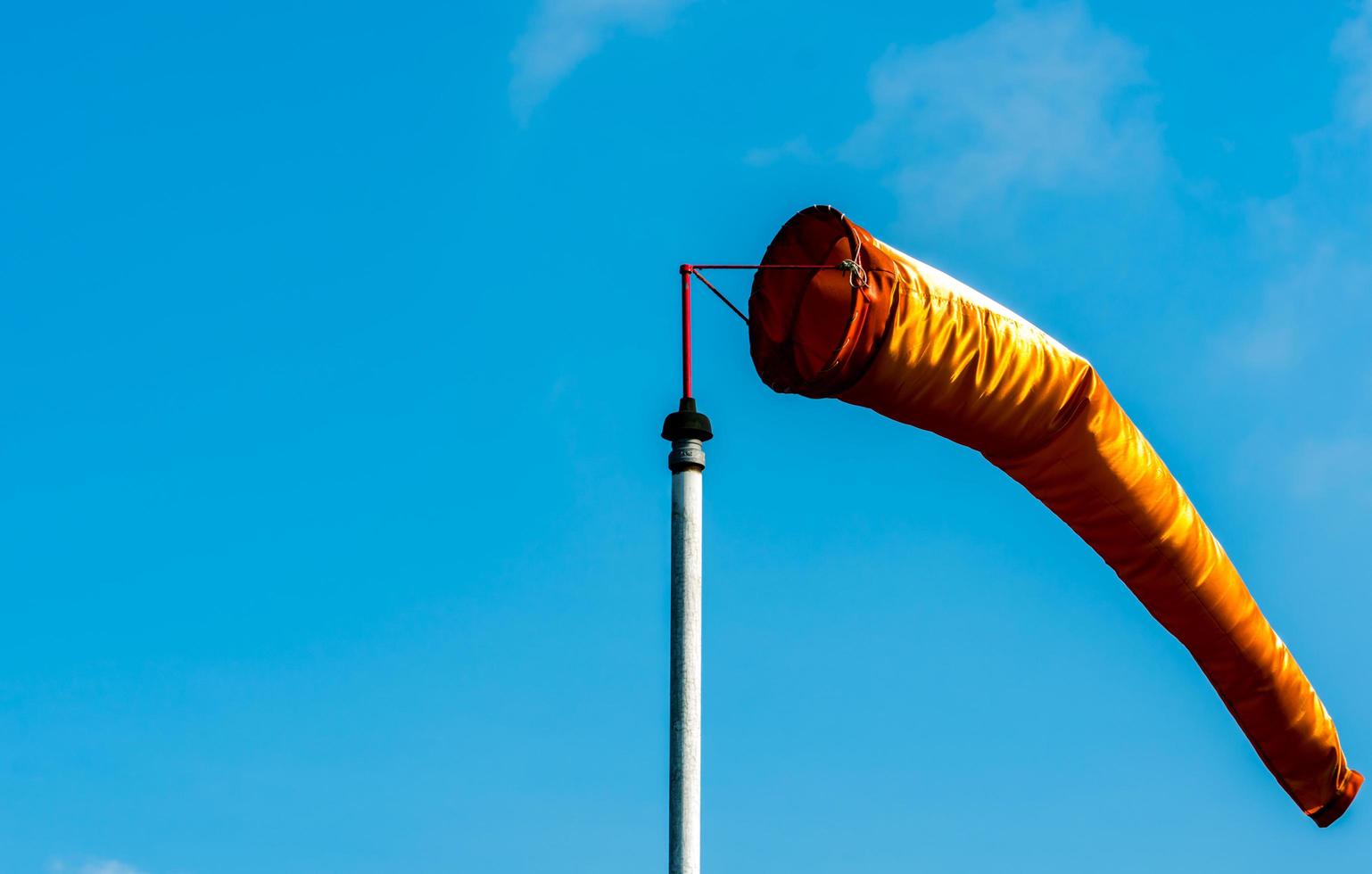 Orange windsock in moderate wind on white pole against clear blue sky on sunny day at aviation area. Wind direction sign at the airport field photo