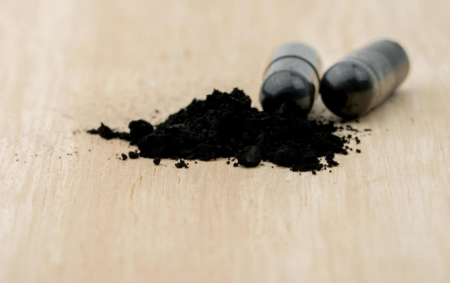 Activated charcoal capsule pills. Selective focus on black powder of activated charcoal on brown wooden table. Medicinal carbon for relieves diarrhea, food or drug poisoning, flatulence. photo