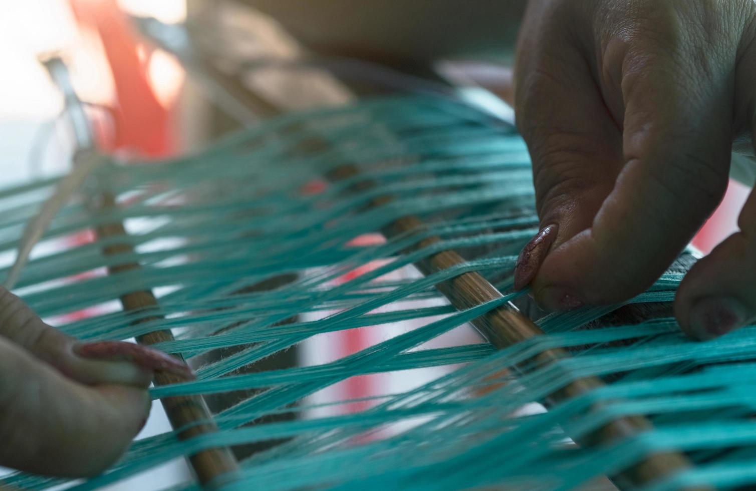 enfoque selectivo en la mano de la mujer sosteniendo hilos de algodón verde en la máquina de tejer para tejer tela hecha a mano. tejido textil. tejido en telar manual tradicional. producción textil o de telas. foto