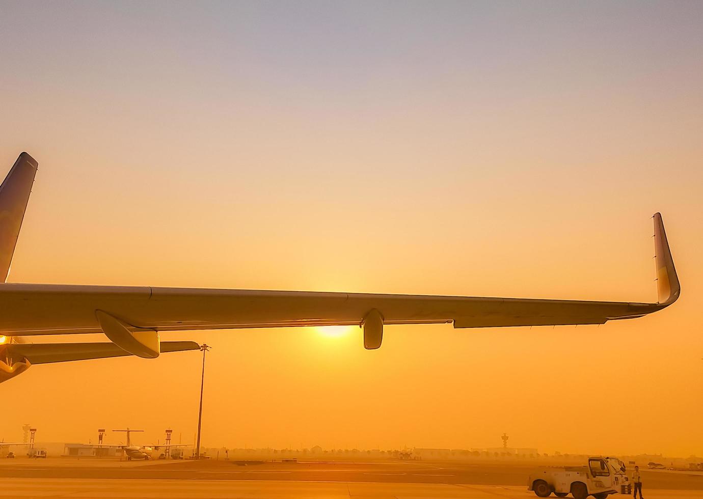 ala de avión de primer plano con cielo dorado del amanecer. avión estacionado en el aeródromo del aeropuerto. vuelo de la mañana. concepto de viaje de verano. apoyo del tractor pushback con personal del aeropuerto en las calles de rodaje. negocio de la aviación. foto