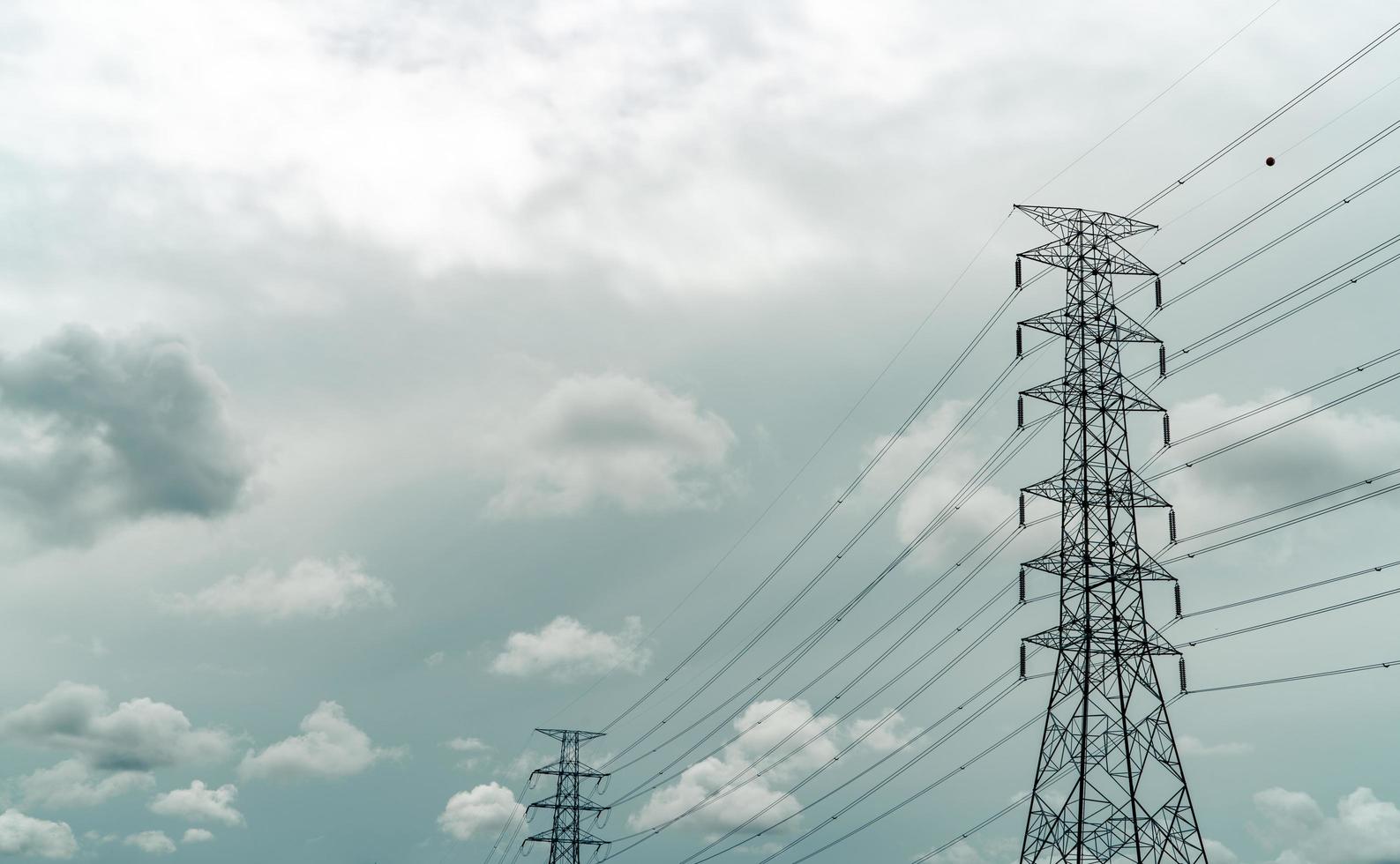 pilón eléctrico de alto voltaje y cable eléctrico con cielo gris y nubes blancas. postes de electricidad concepto de potencia y energía. torre de red de alto voltaje con cable de alambre. infraestructura. distribución de poder foto