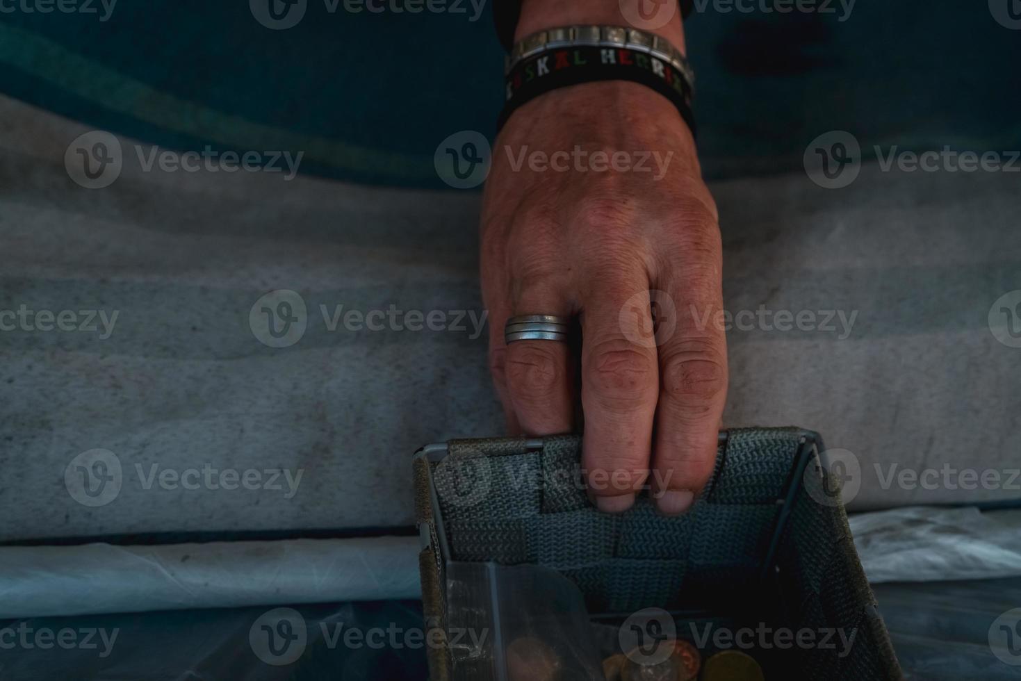 Homeless hand with small basket with coin on the street. Beggar begging for money. Poor man sit on bed in winter beside the street. Poverty and social problems. Poor and sad man need money and help. photo