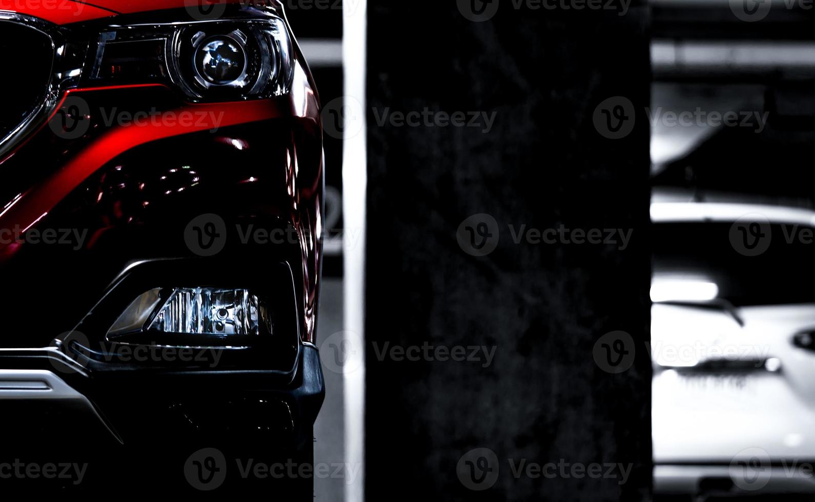 Closeup headlights of red SUV sport car parked near concrete pole at indoor parking lot. Headlamp lights with elegant and luxury design. Automotive industry and hybrid car concept. Underground parking photo