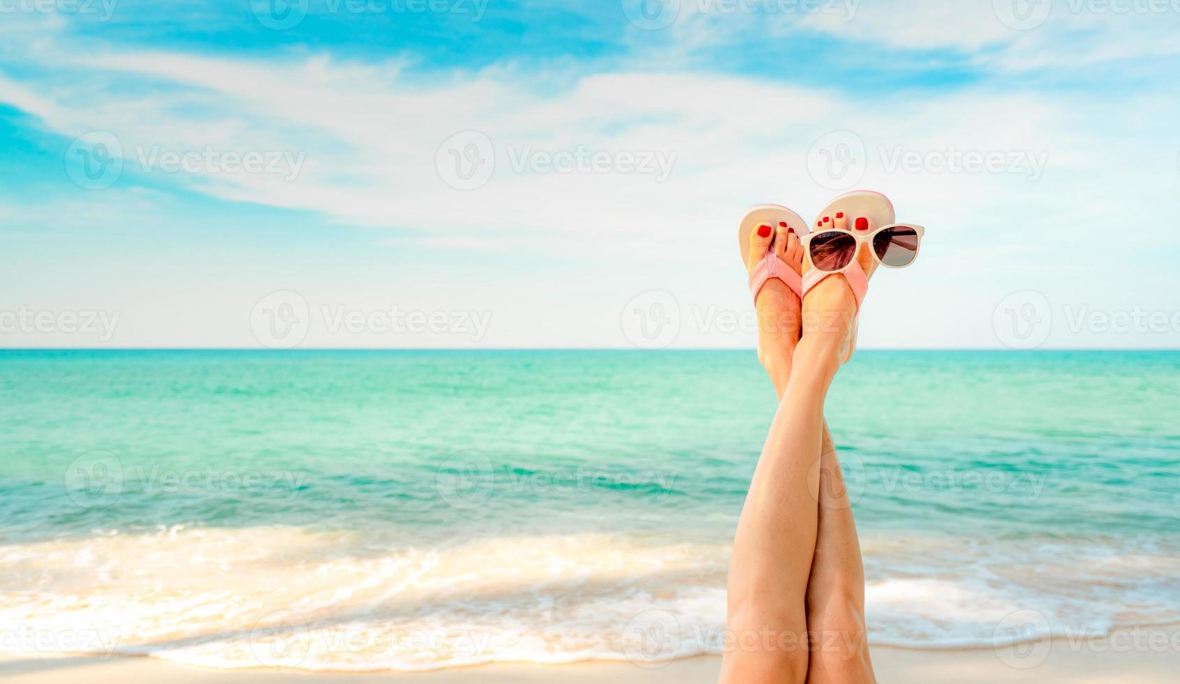 Upside woman feet and red pedicure wear pink sandals, sunglasses at seaside. Funny and happy fashion young woman relax on vacation. Girl on beach. Creative for tour agent. Weekend travel. Summer vibes photo