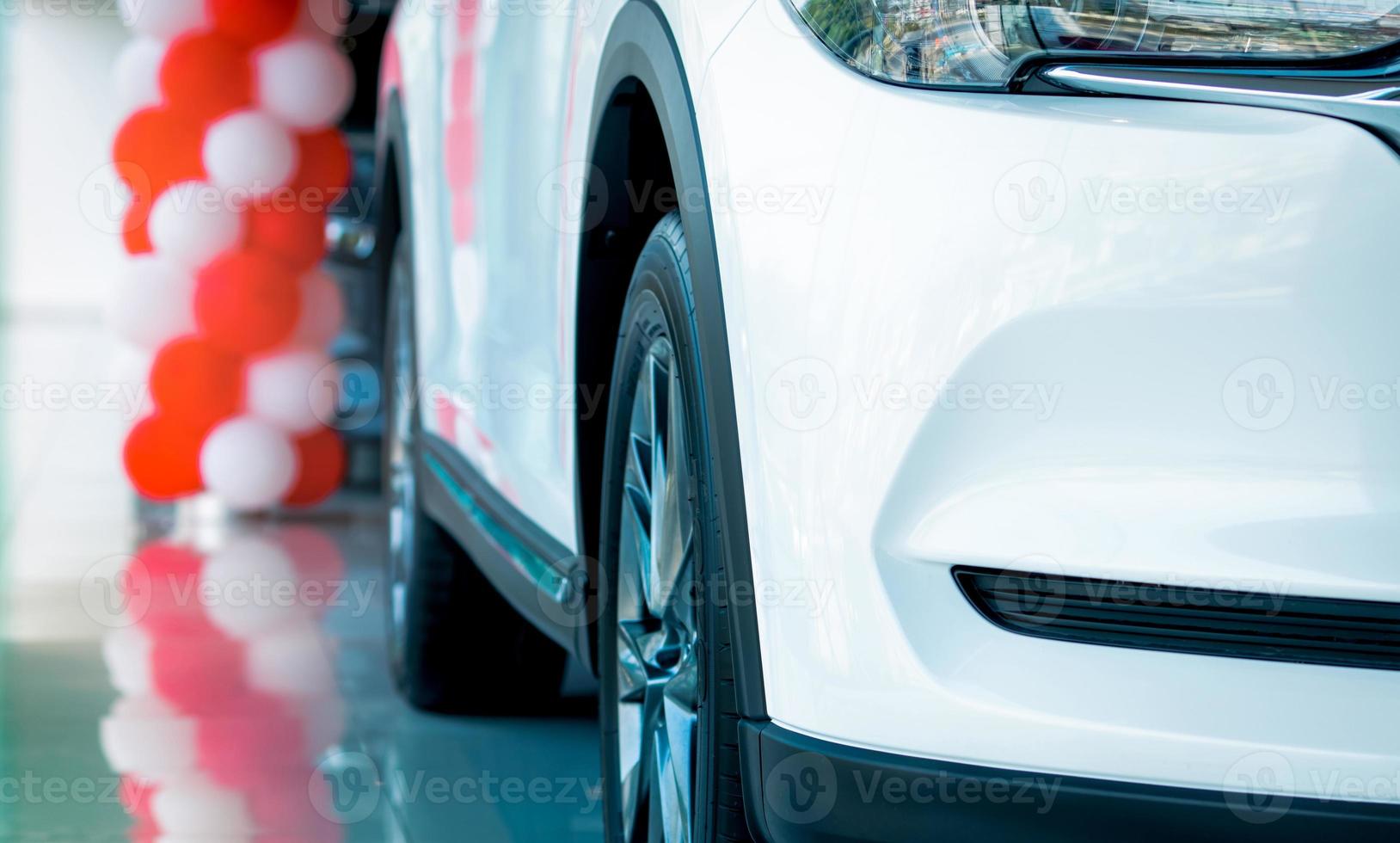 Closeup grille and wheel of new white luxury SUV car parked in modern showroom. Car dealership showroom office. Automobile leasing concept. Automotive industry. Electric and hybrid car industry. photo