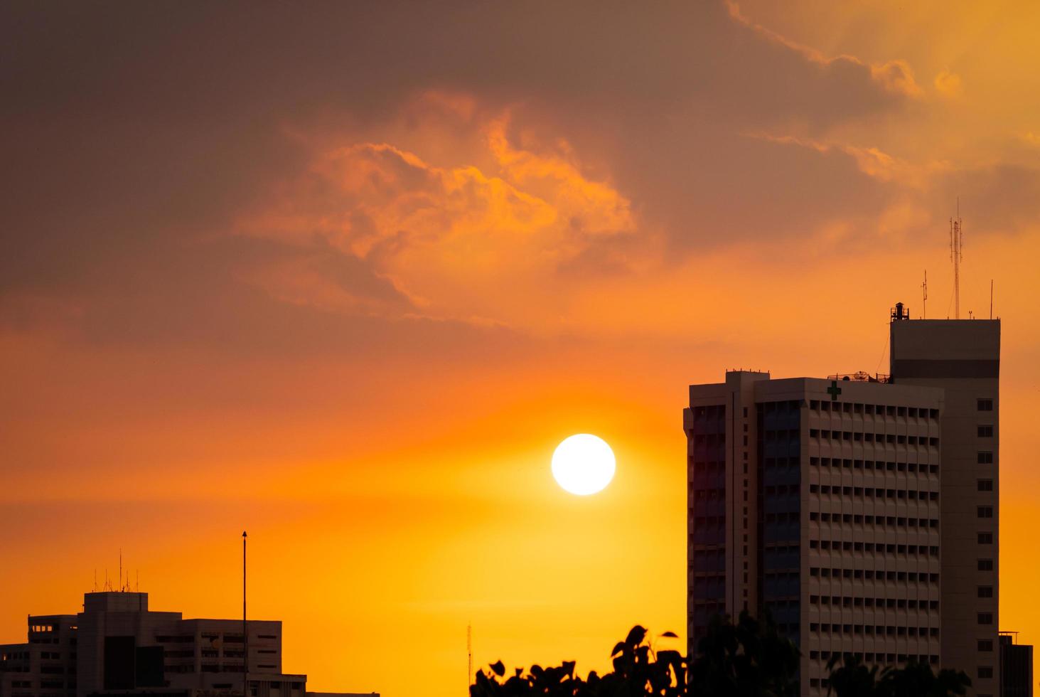Hospital building at dusk with beautiful sunset sky. Silhouette of hospital building in the evening. Cityscape of skyscraper building. Big sun with golden sky and grey clouds at sunset. photo