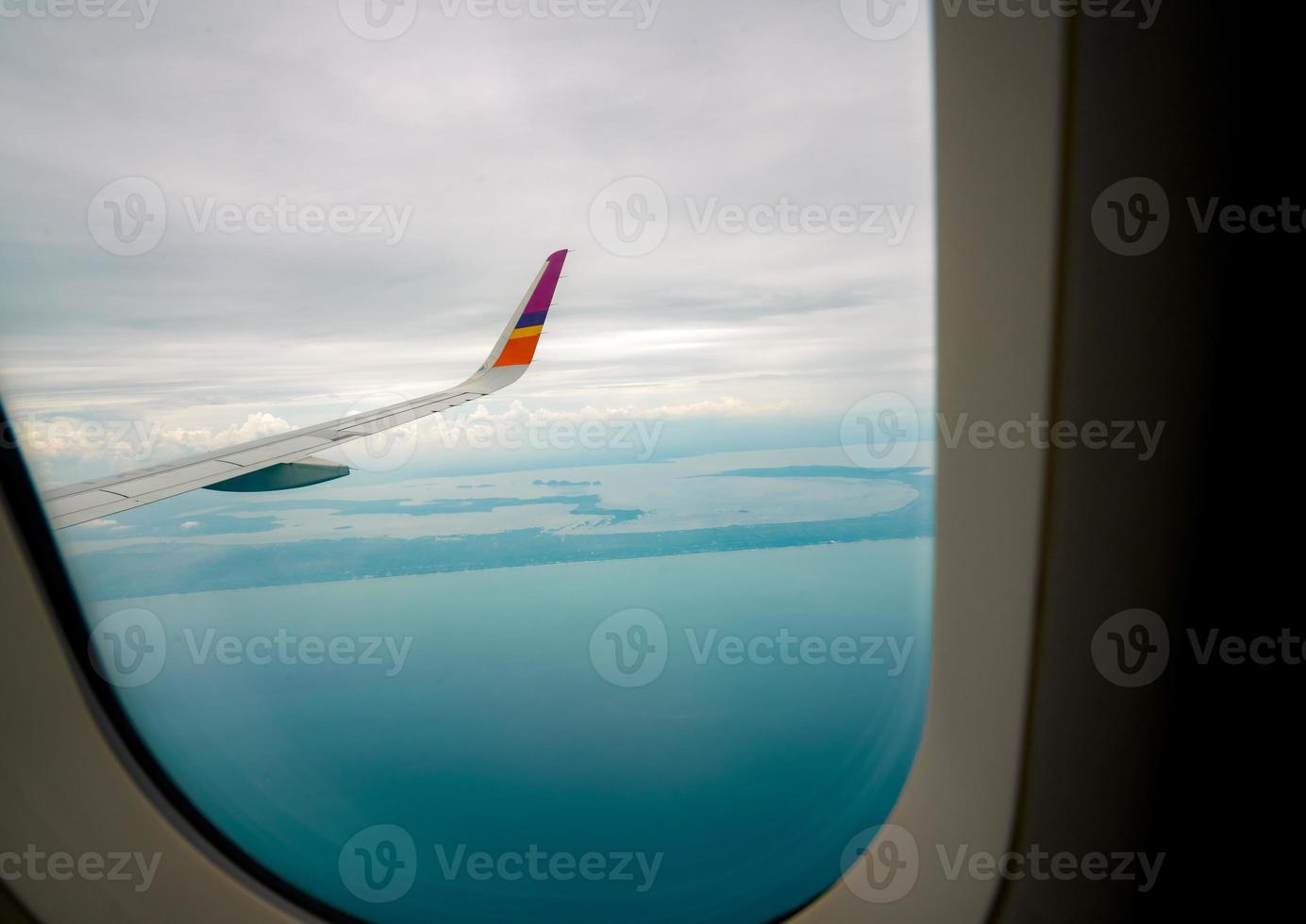 Wing of plane over the city. Airplane flying on blue sky. Scenic view from airplane window. Commercial airline flight with white clouds sky and blue sea beach. Plane wing above tropical beach. photo