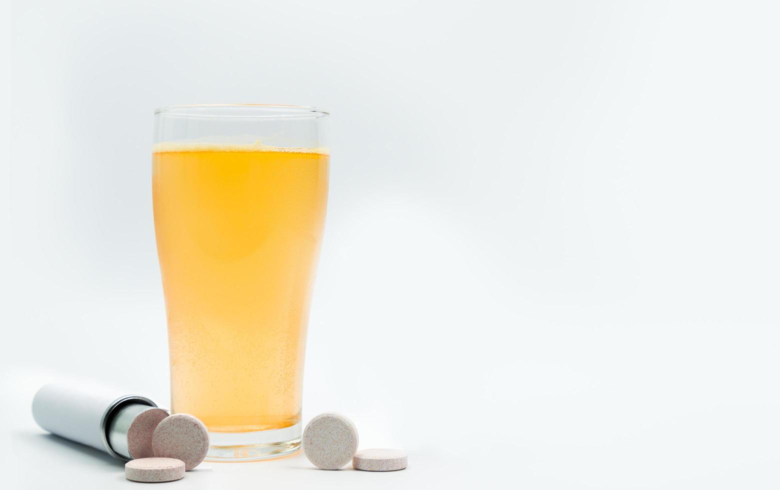 Effervescent tablets tube with blank label and orange effervescent bubbles of calcium and vitamin C in transparent glass. Vitamins, minerals and supplement concept. photo