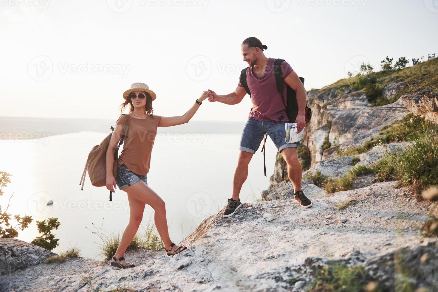 Two tourist with backpacks climb to the top of the mountain and enjoying sunrise photo