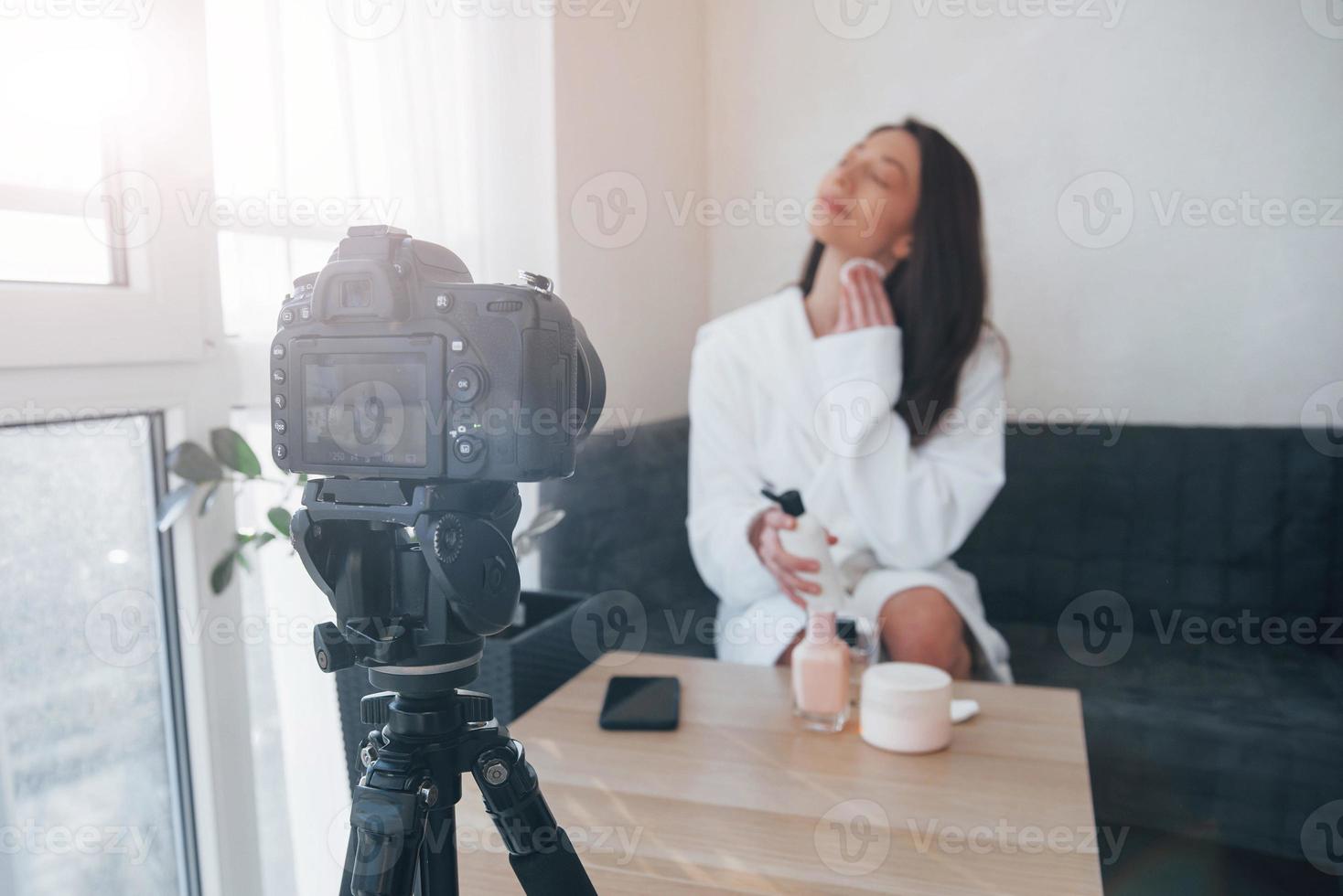 Backstage of the photoshoot. In front of camera on the tripod. Conception of fashion and skincare. Brunette girl uses cosmetics photo