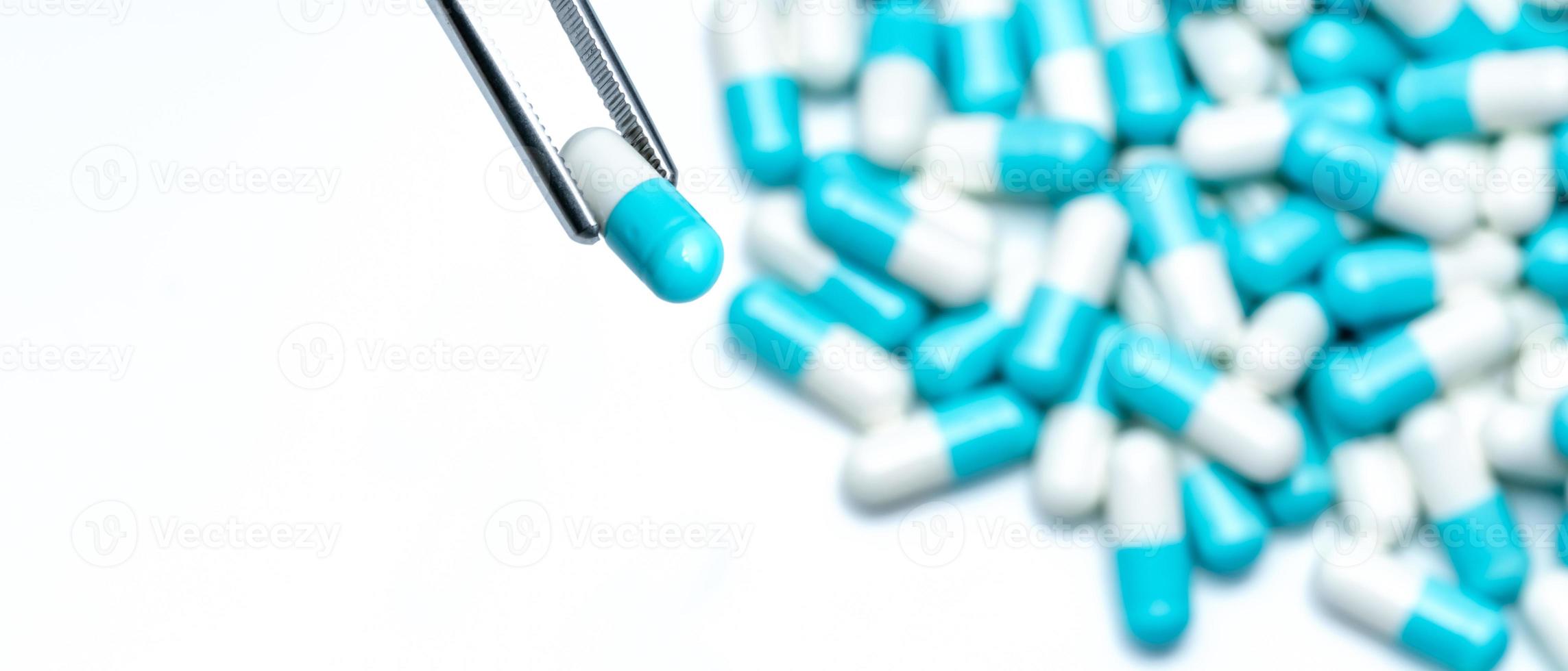 Forceps pick white-blue capsule from group of capsule pills. Drugs choose. Antibiotic drug selection. Antibiotic drug resistance concept. QA and QC in pharmaceutical factory concept. Drugs of choice. photo