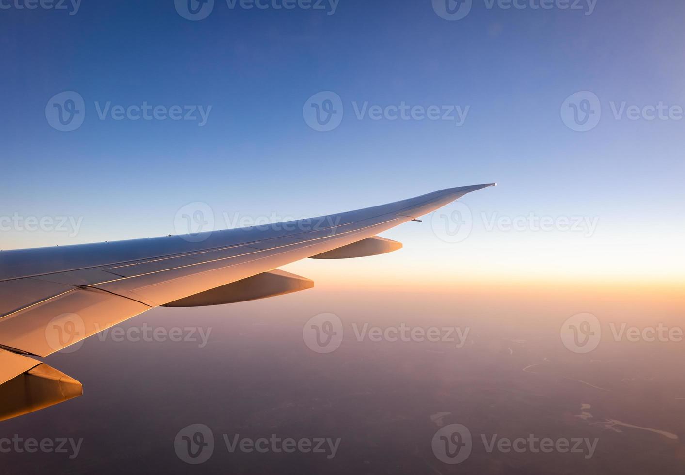 Wing of plane over the city. Airplane flying on blue sky. Scenic view from airplane window. Commercial airline flight in the morning with sunlight. Plane wing above clouds. Flight mechanics concept. photo