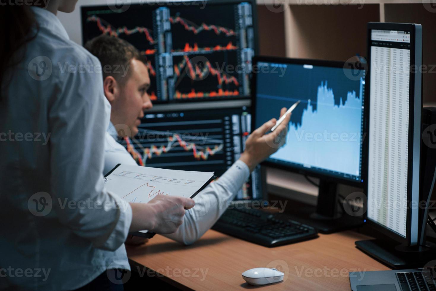 Man shows results. Team of stockbrokers are having a conversation in a office with multiple display screens photo