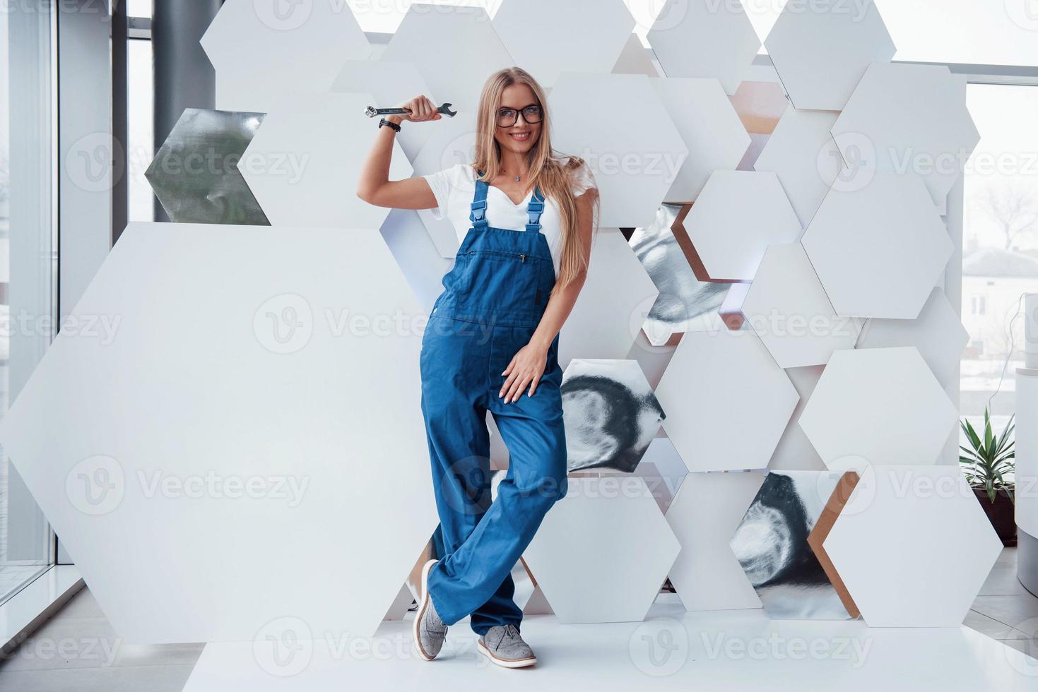 A silver colored instrument. Girl in blue uniform stands against abstract wall with white pieces of surface in the shape of hexagon in the auto saloon photo