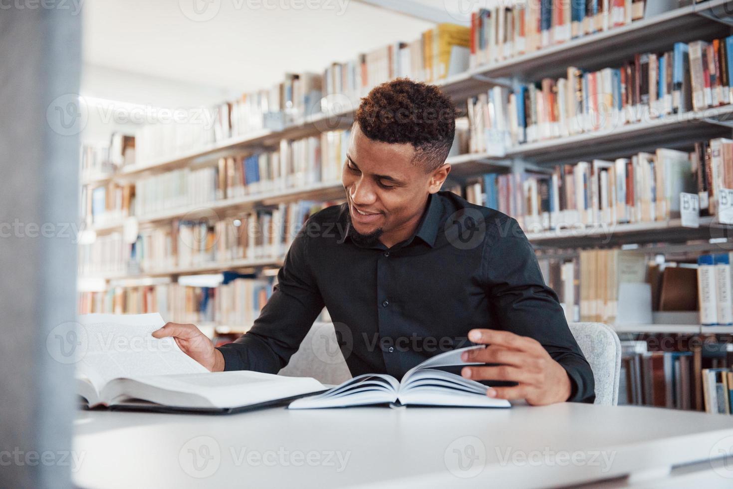 Smiling during the process. African american man sitting in the library and searching for some information in the books photo