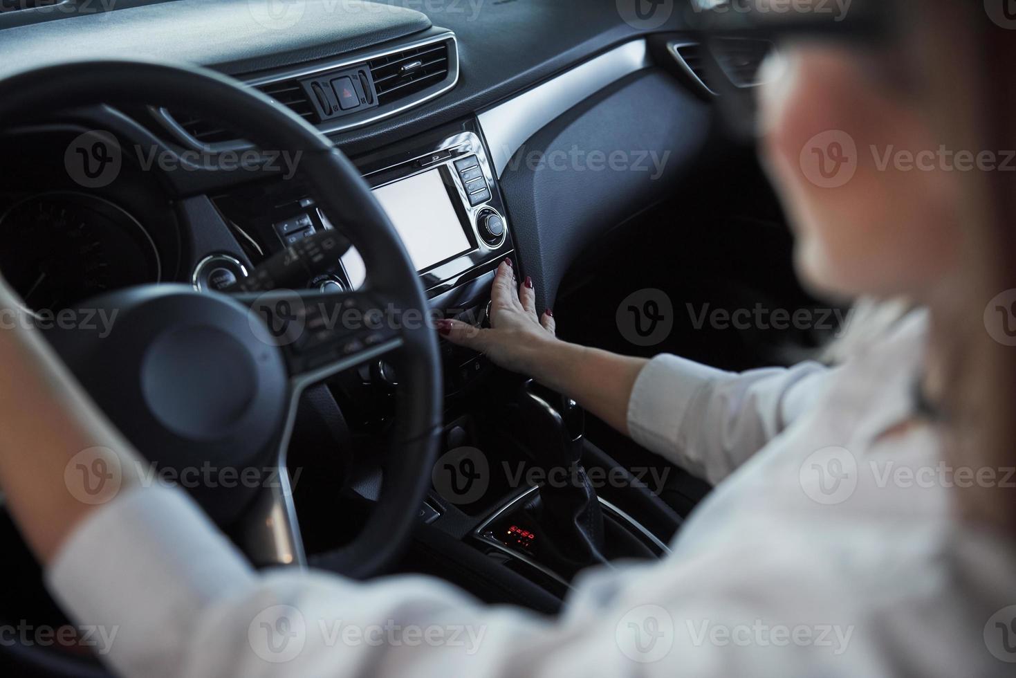 presionando los botones. hermosa chica rubia sentada en el auto nuevo con interior negro moderno foto