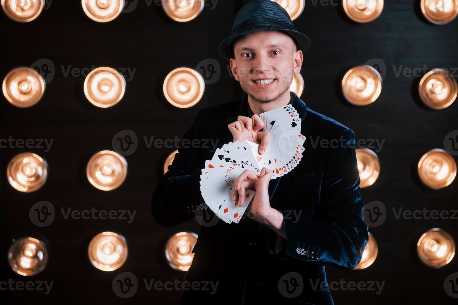 Your turn to pick. Magician in black suit and with playing cards standing in the room with special lighting at backstage photo