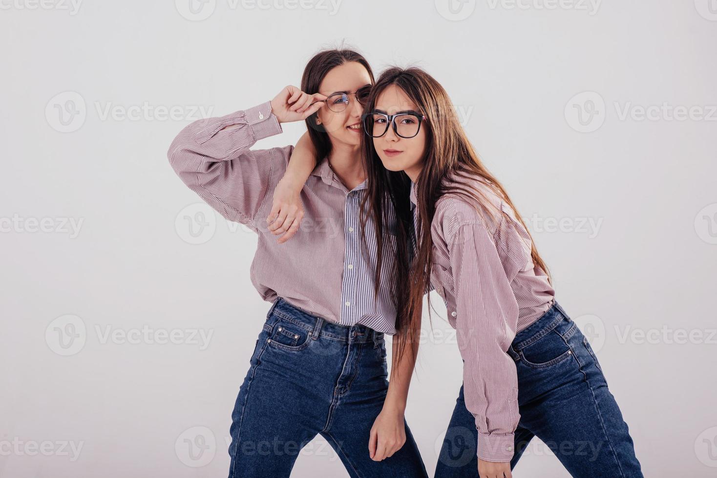 Cheerful atmosphere. Two sisters twins standing and posing in the studio with white background photo