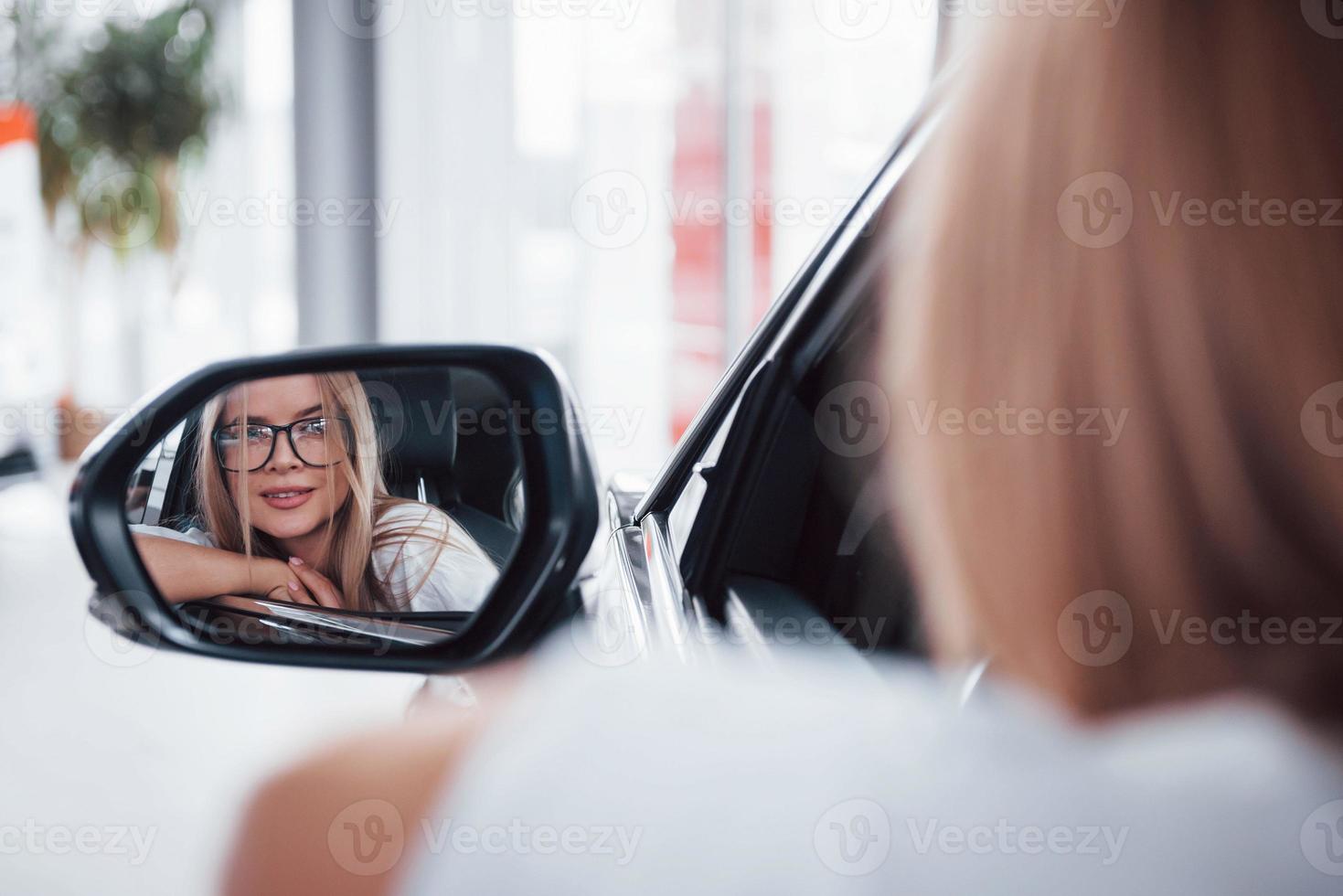 From the mirror. Woman in glasses looking into side mirror of a modern vehicle in the saloon photo