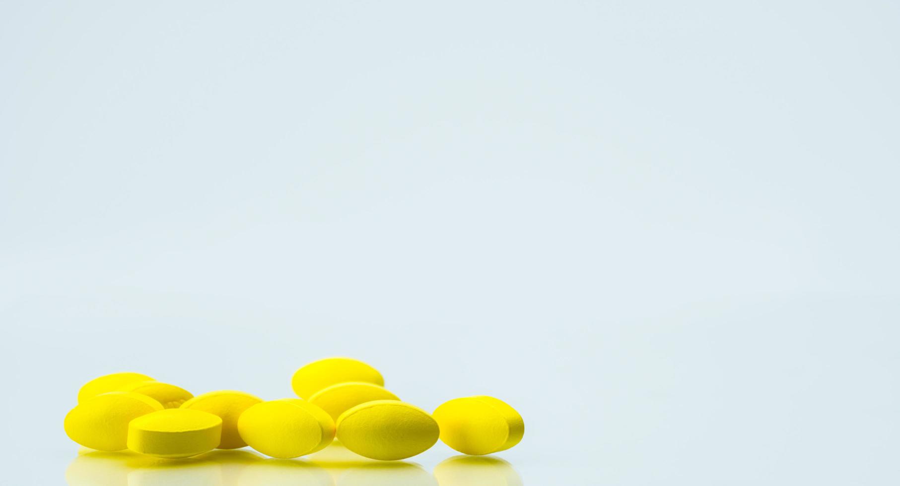 Pile of yellow oval tablet pills on white background with copy space for text. Mild to moderate pain management. Pain killer medicine. photo