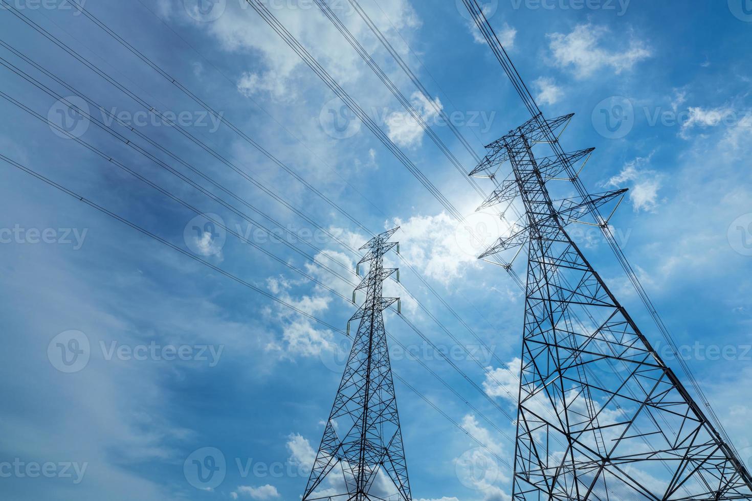 High voltage electric pylon and electrical wire against blue sky and white clouds. Bottom view of Electricity pylon with sunlight. High voltage grid tower with wire cable.  Power and energy concept. photo