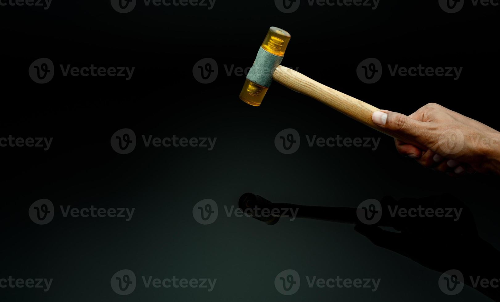 Man's hand holding plastic hammer isolated on dark background. Male worker's hand hold wood handle of plastic hammer. Hammer head made of soft and tough yellow plastic that not damage workpiece. photo