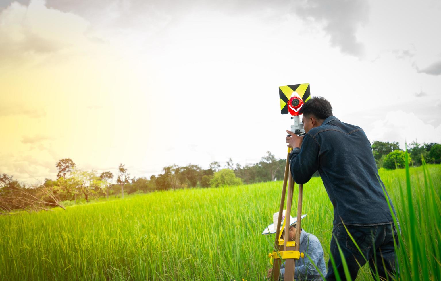 Asian smart engineer or surveyor in black jeans and long sleeve shirt  are measuring the lands of rice field by Theodolite. photo
