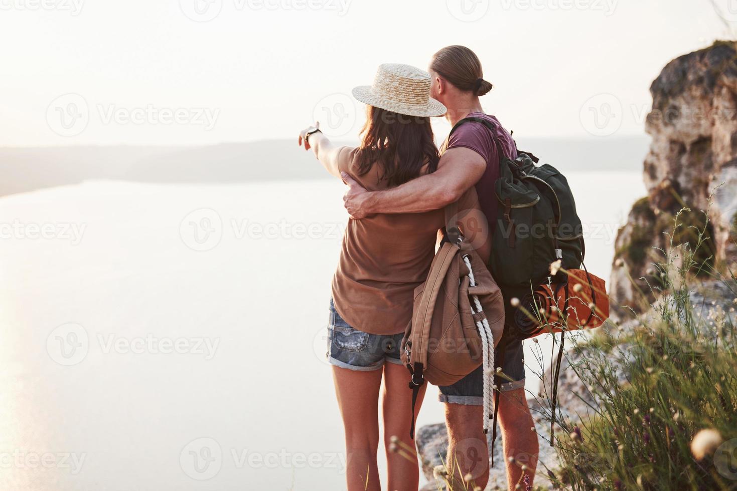 Two tourist male and woman with backpacks stand to the top of the mountain and enjoying sunrise. Travel lifestyle adventure vacations concept photo