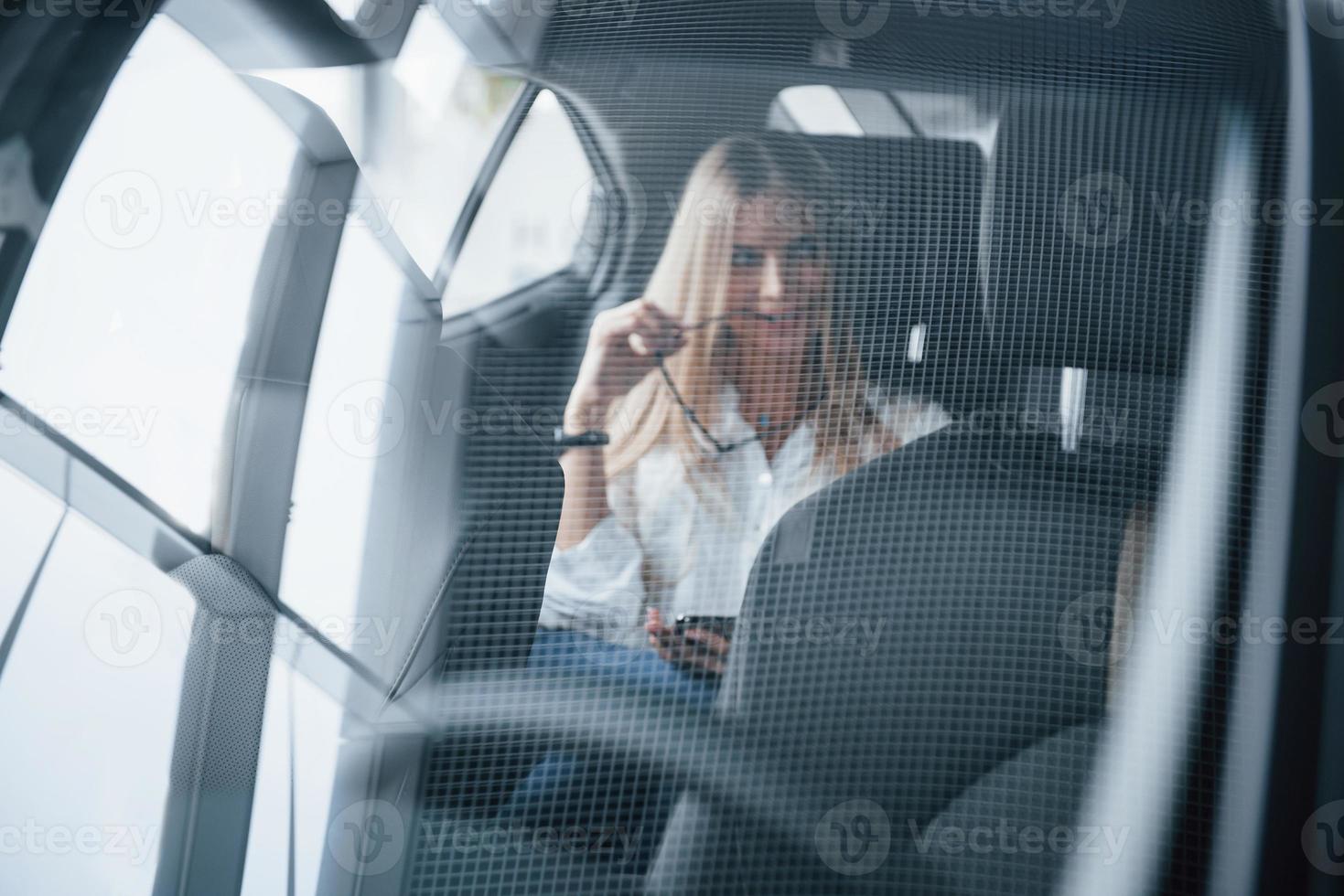 Through the glass with reflection of ceiling. Smart businesswoman sits at backseat of the luxury car with black interior photo