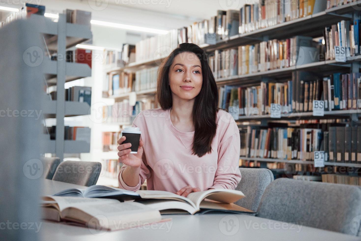 Looking forward. Brunette girl in casual clothes having good time in the library full of books photo