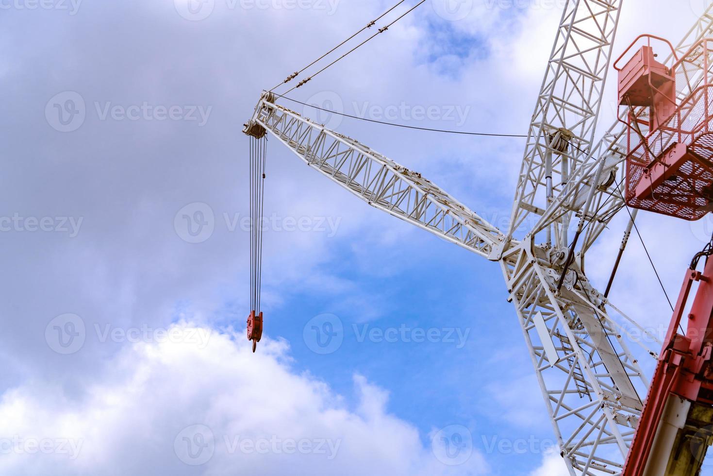 Crawler crane against blue sky and white clouds. Real estate industry. Red-white crane use reel lift up equipment in construction site. Crane for rent. Crane dealership for construction business. photo