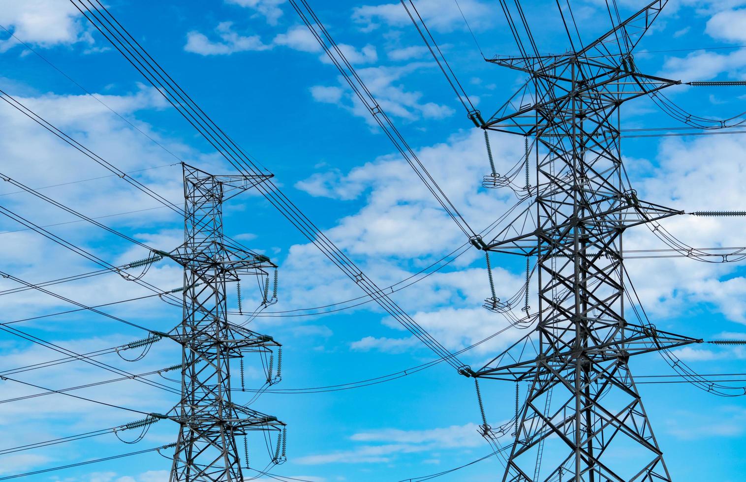 High voltage electric pylon and electrical wire against blue sky and clouds. Bottom view of electric pylon. High voltage grid tower with wire cable. Transmission lines on high voltage grid tower. photo