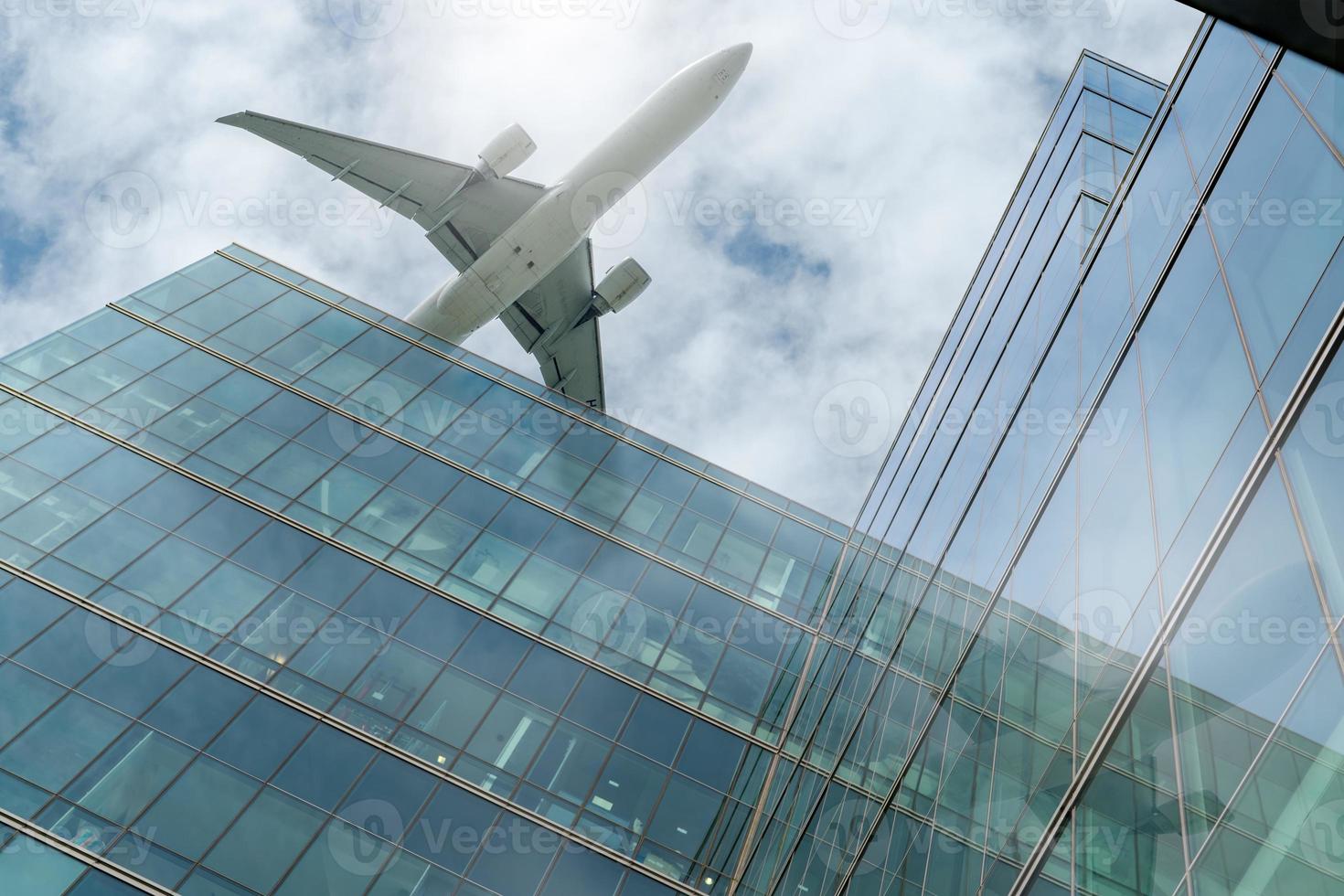 Airplane flying above modern office building. Exterior facade of skyscraper building. Business trip. Reflection in transparent glass windows. Aviation business after coronavirus vaccine injection. photo