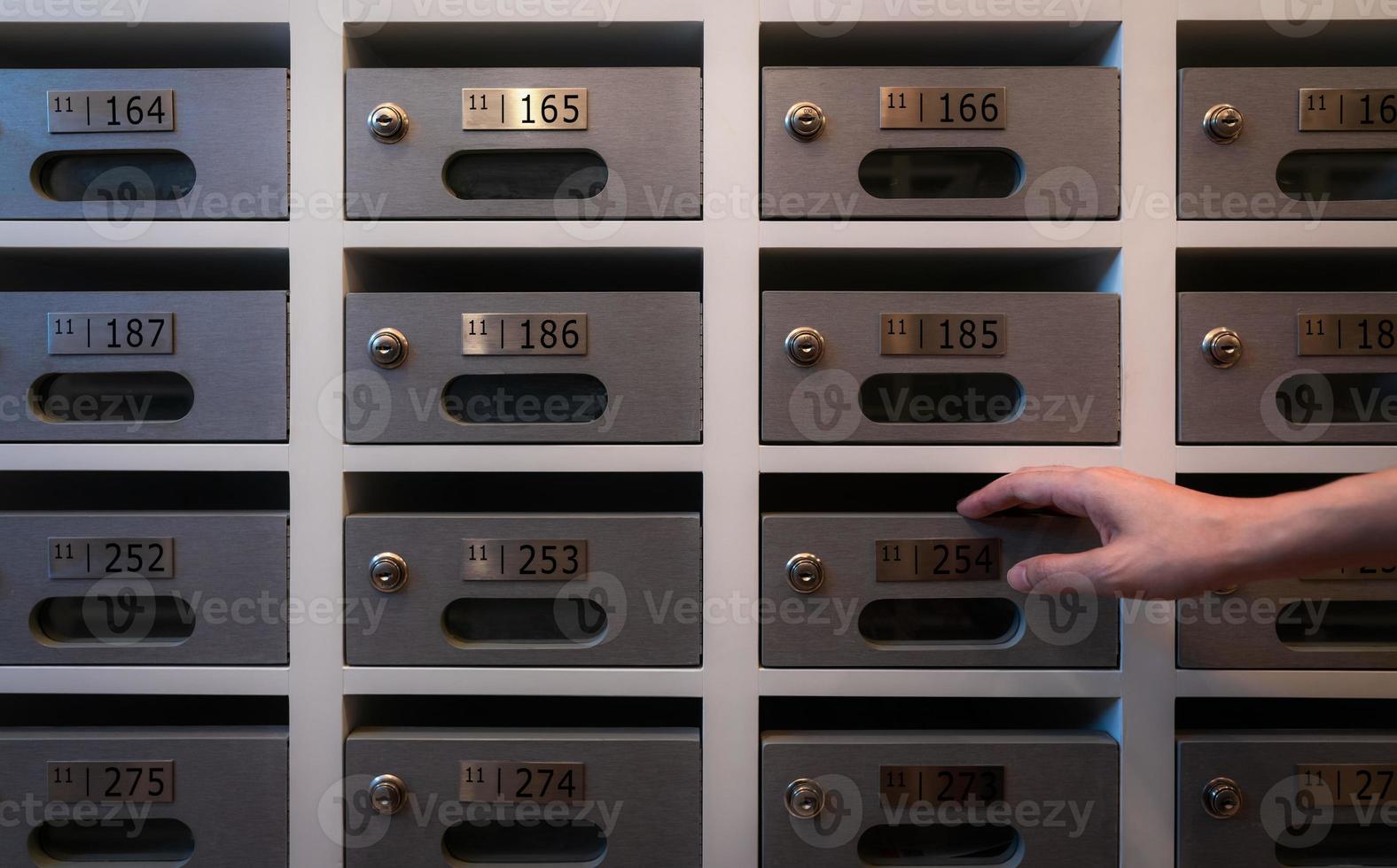 Woman hand open modern mail box of apartment filled home numbers of resident. Mailbox in a row in letter box office of apartment. Post office and envelope mail delivery business concept. Postbox lock. photo