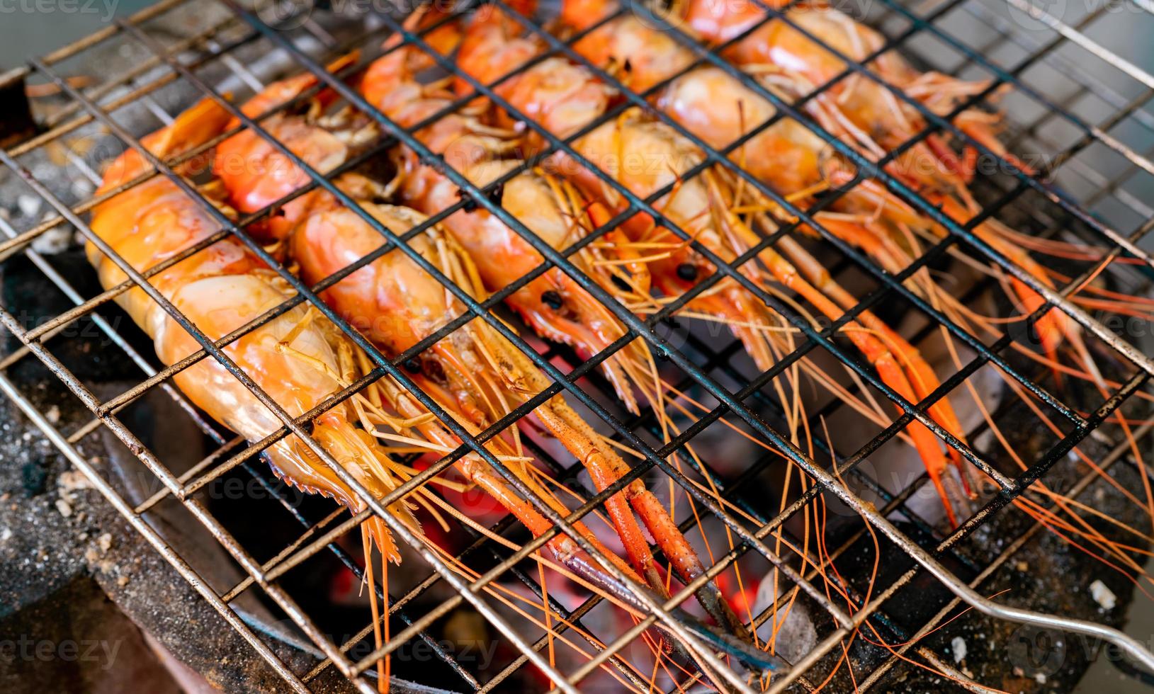 Grilled prawn on charcoal grill. Giant freshwater prawns grill on a flaming charcoal fire. Closeup giant river prawn cooking on barbecue grill rack. Cooking food for the party. Thai food culture. photo