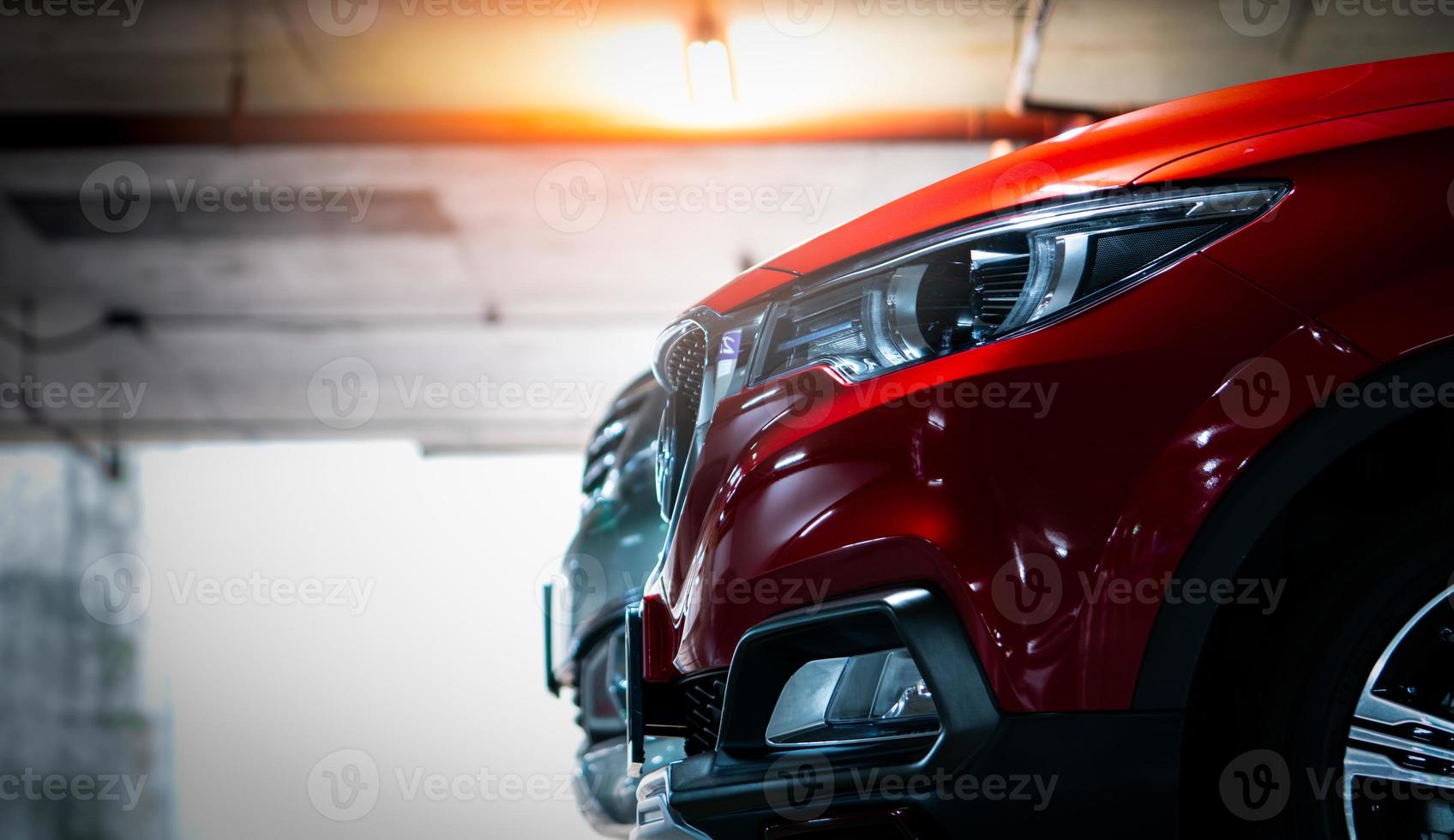 Selective focus on red shiny SUV sport car parked at shopping mall indoor parking lot. Headlamp lights with elegant and luxury design. Automotive industry and hybrid car concept. Underground parking. photo