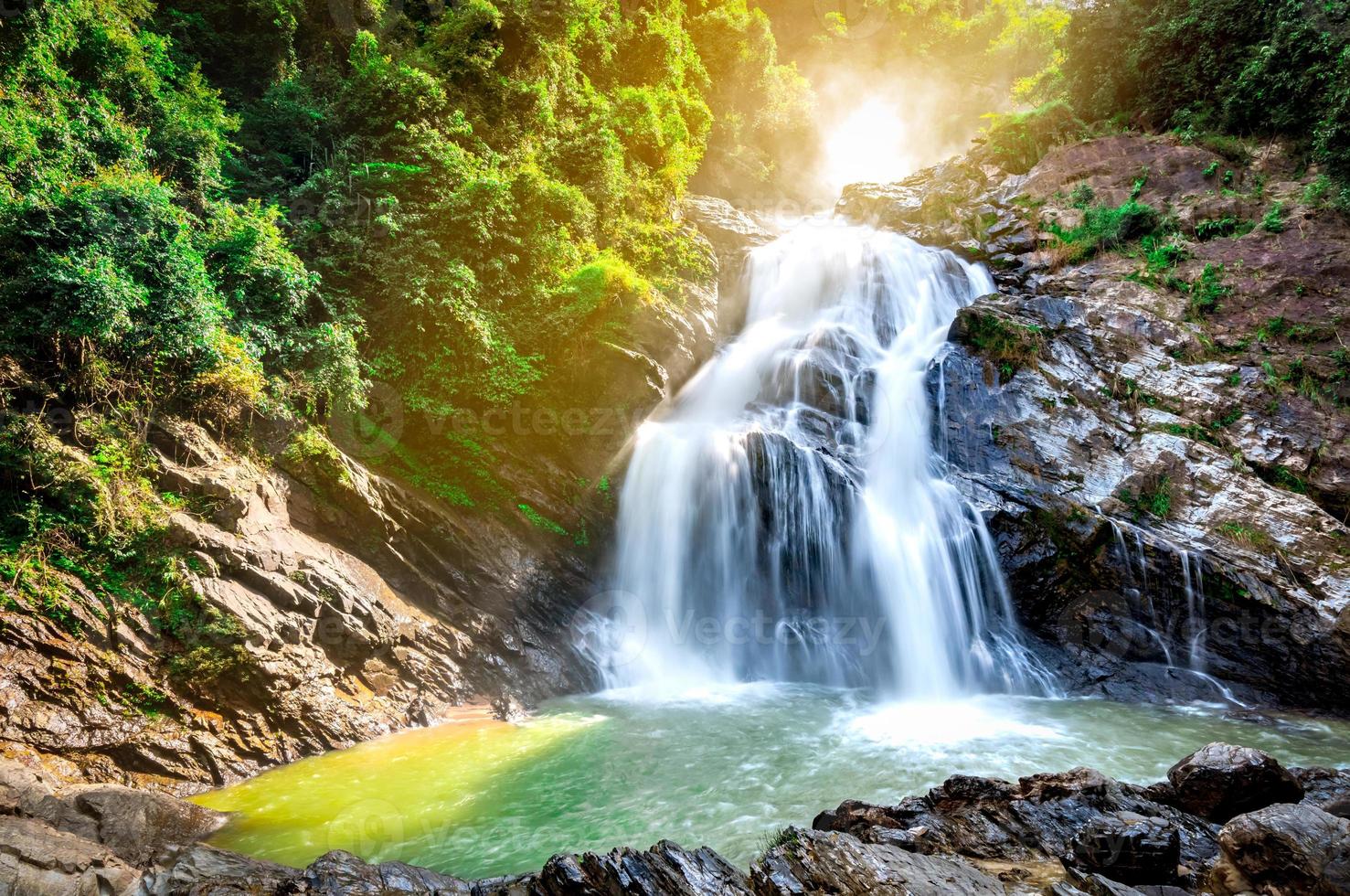 Beautiful waterfall at the mountain with blue sky and white cumulus clouds. Waterfall in tropical green tree forest. Waterfall is flowing in jungle. Nature abstract background. Granite rock mountain. photo