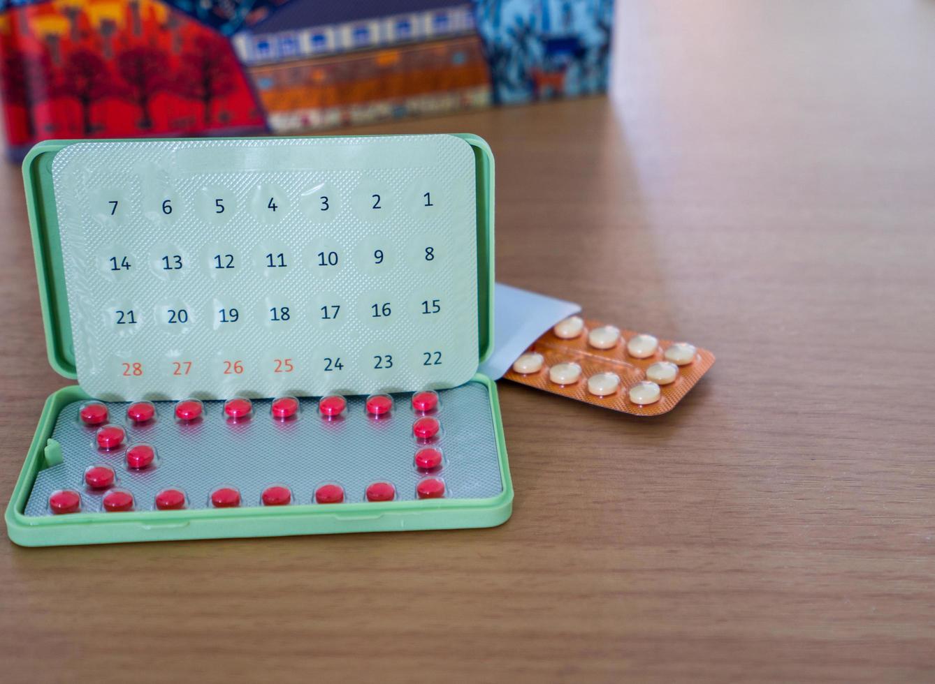 Contraceptive pills with modern packaging on the brown wood work table beside notebook. Birth control pills in blister pack. Family planning. Hormones tablet pills. Pharmacy products. Woman hormones. photo